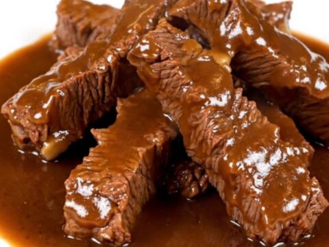 A bowl filled with tender beef tips covered in a rich, dark brown gravy with visible onion slices.