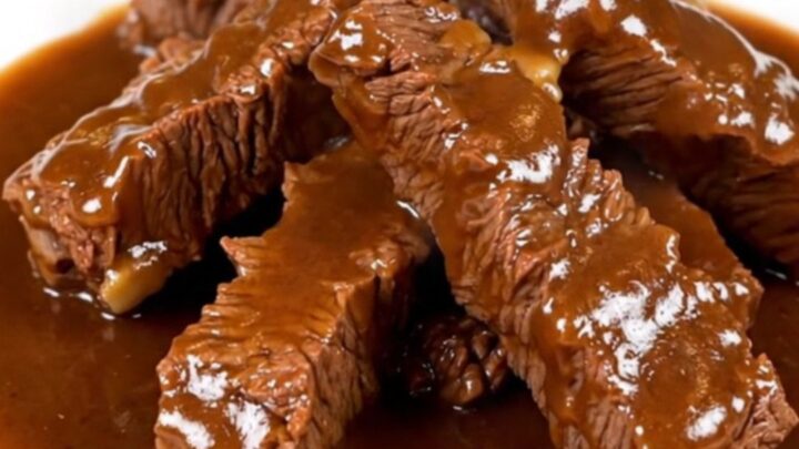 A bowl filled with tender beef tips covered in a rich, dark brown gravy with visible onion slices.