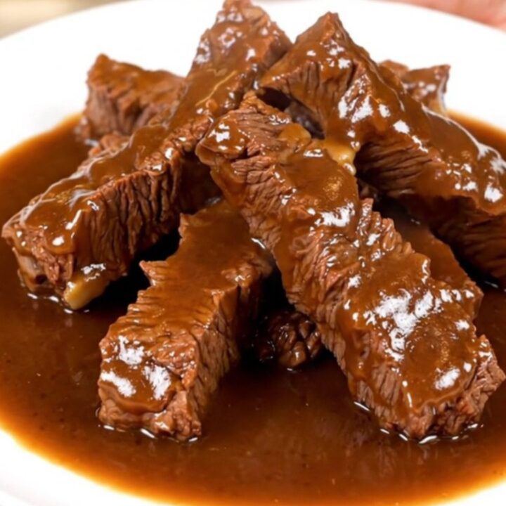 A bowl filled with tender beef tips covered in a rich, dark brown gravy with visible onion slices.