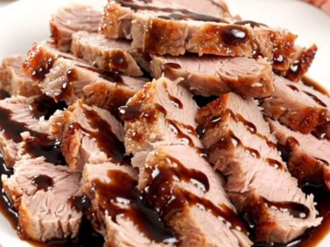 A close-up of tender, sliced balsamic fig pork tenderloin drizzled with a glossy reduction on a white plate.