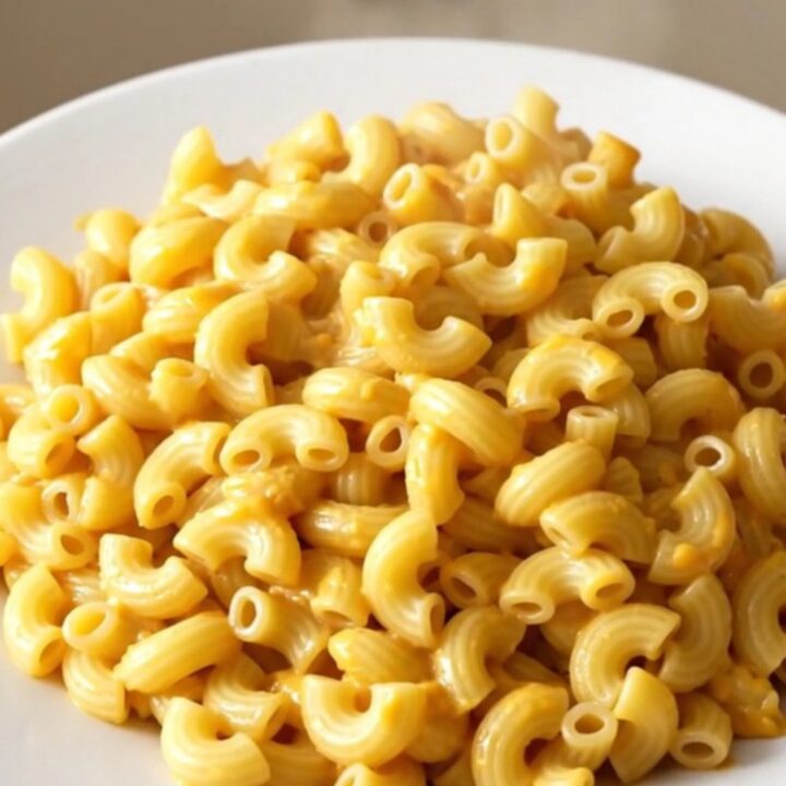 A bowl of creamy pimento cheese macaroni with visible bits of red pimento scattered throughout.