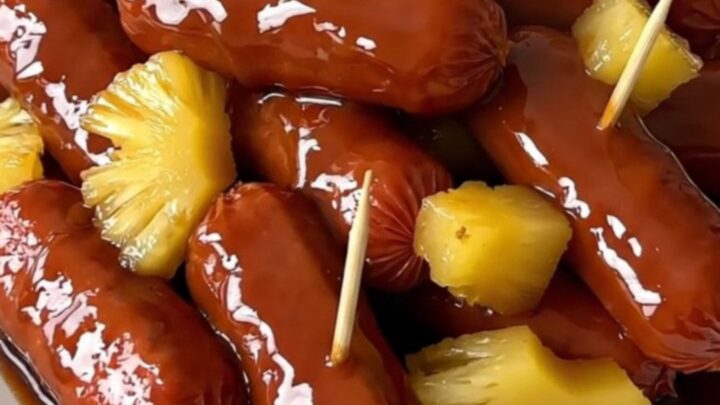 A close-up of glossy, glazed cocktail smokies and pineapple chunks on a white plate.