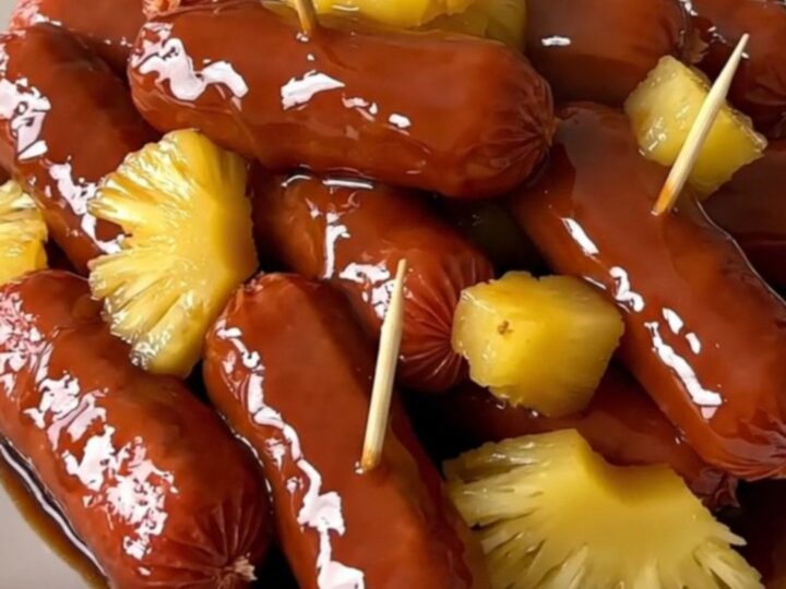 A close-up of glossy, glazed cocktail smokies and pineapple chunks on a white plate.