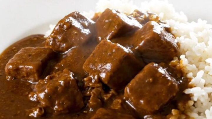 A top-down view of a slow cooker filled with beef, potatoes, carrots, and onions, with curry cubes added on top.
