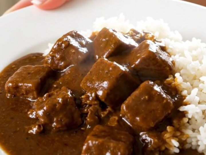 A top-down view of a slow cooker filled with beef, potatoes, carrots, and onions, with curry cubes added on top.
