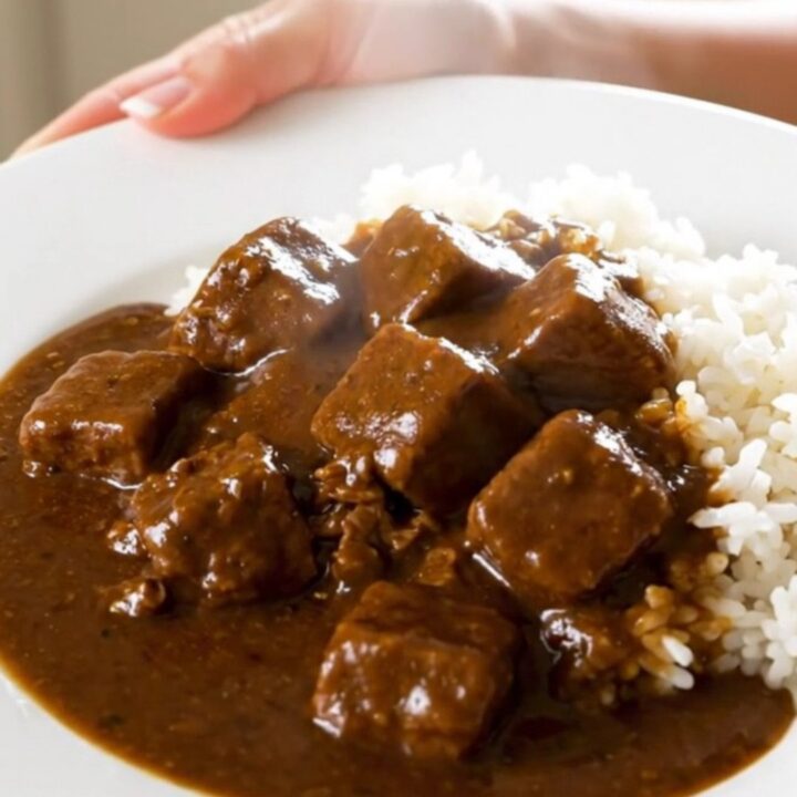 A top-down view of a slow cooker filled with beef, potatoes, carrots, and onions, with curry cubes added on top.