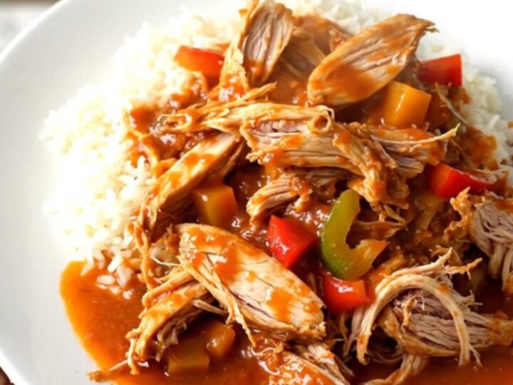A slow cooker filled with raw chicken breasts, sliced peppers, onions, and crushed tomatoes.