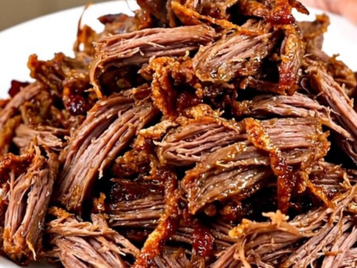 A close-up of tender, shredded beef carnitas on a white plate with fresh garnishes.