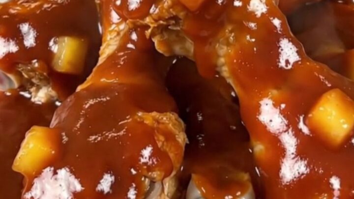 Slow cooker filled with cooked chicken drumsticks coated in a rich, glossy pineapple barbecue sauce.