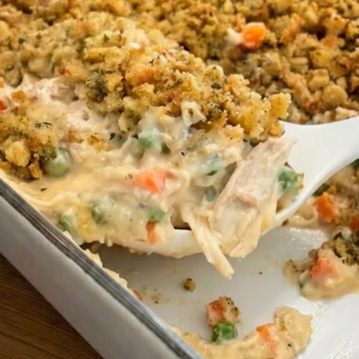 A close-up of a white spoon scooping creamy chicken and vegetable casserole with a crunchy herb stuffing topping.