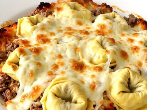 A steaming, glossy portion of cheesy beef tortellini bake served on a white plate.