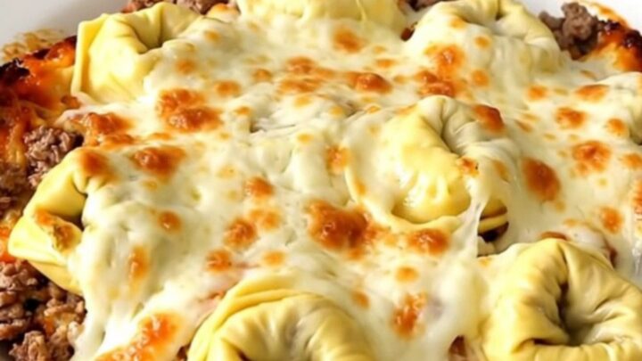 A steaming, glossy portion of cheesy beef tortellini bake served on a white plate.