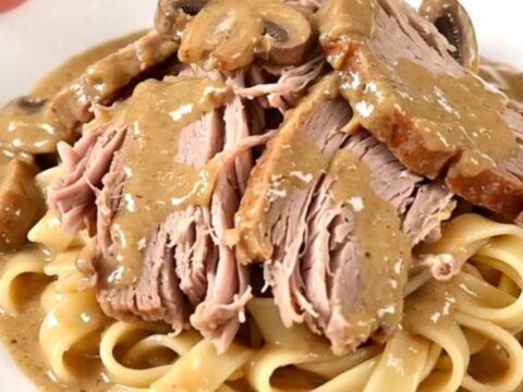 A tender, slow-cooked pork roast smothered in a creamy mushroom and herb sauce on a white plate.