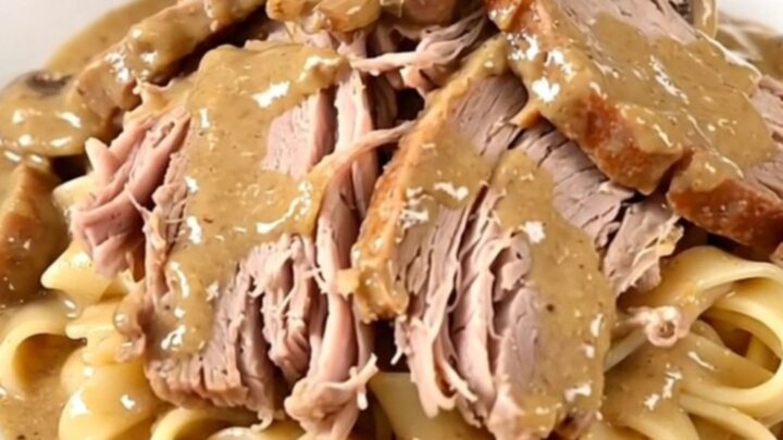 A tender, slow-cooked pork roast smothered in a creamy mushroom and herb sauce on a white plate.