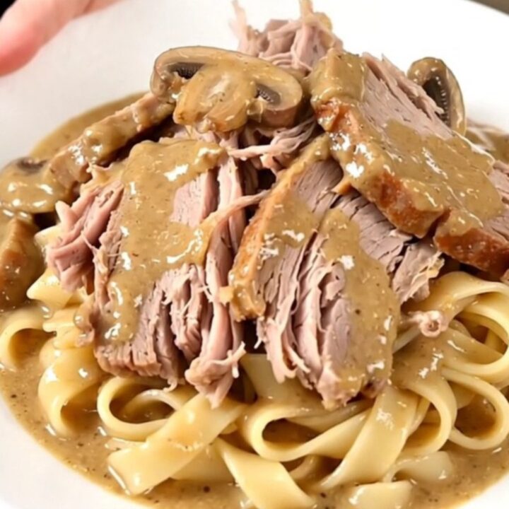 A tender, slow-cooked pork roast smothered in a creamy mushroom and herb sauce on a white plate.