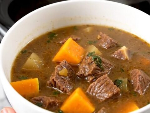 A close-up view of beef and butternut squash stew in a white bowl with steam rising.