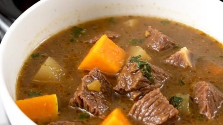 A close-up view of beef and butternut squash stew in a white bowl with steam rising.