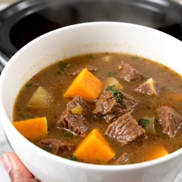 A close-up view of beef and butternut squash stew in a white bowl with steam rising.