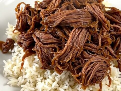 A close-up of tender, shredded beef in a dark, glossy sweet and sour sauce served on a clean white plate.