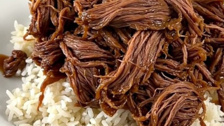 A close-up of tender, shredded beef in a dark, glossy sweet and sour sauce served on a clean white plate.