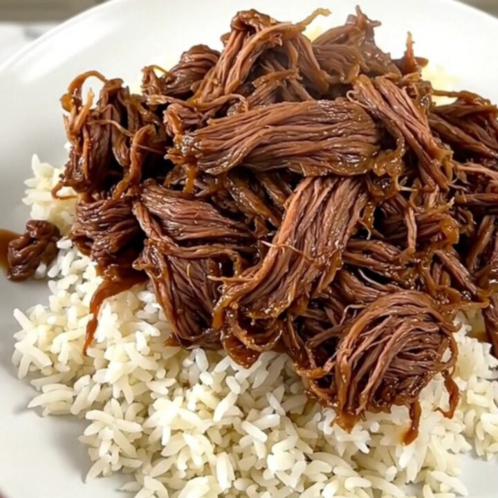A close-up of tender, shredded beef in a dark, glossy sweet and sour sauce served on a clean white plate.