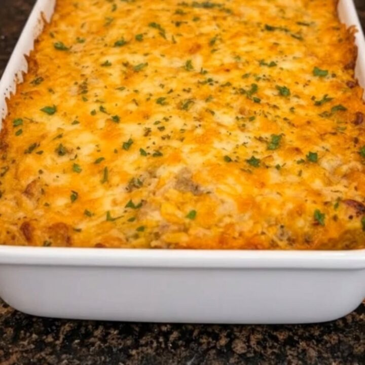 A steaming white rectangular dish filled with golden-brown cheesy chicken and rice casserole on a dark granite counter.