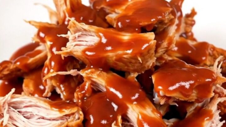 A top-down view of raw chicken thighs, onions, and gochujang sauce inside a black oval slow cooker on a white countertop.