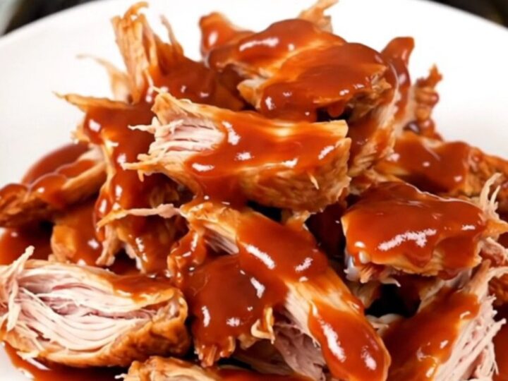 A top-down view of raw chicken thighs, onions, and gochujang sauce inside a black oval slow cooker on a white countertop.