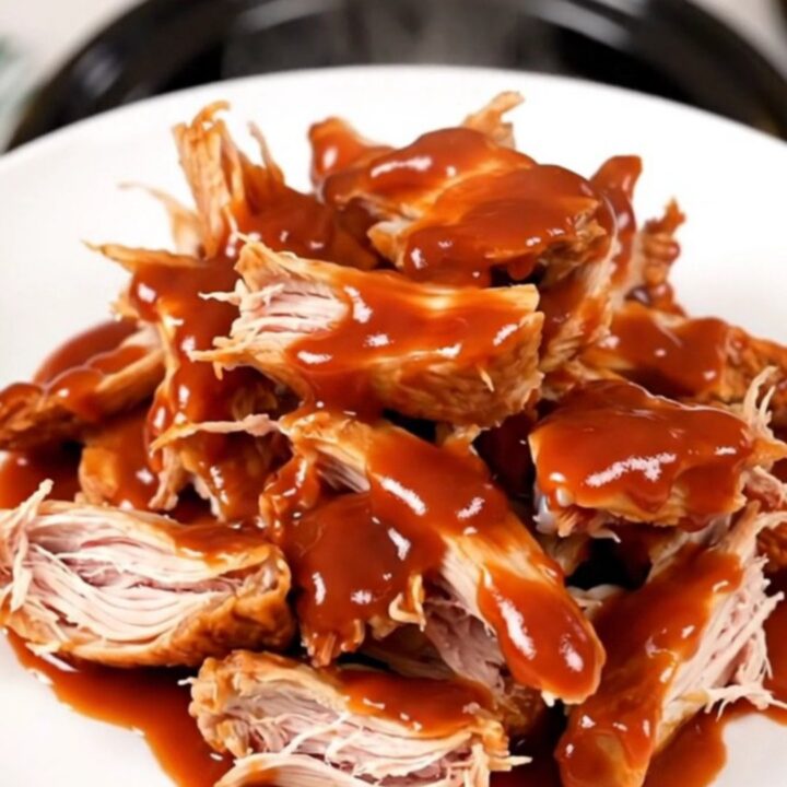A top-down view of raw chicken thighs, onions, and gochujang sauce inside a black oval slow cooker on a white countertop.