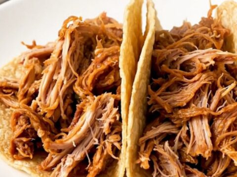 A close-up of finished Mexican shredded turkey tacos on a white plate with a blurry kitchen background.