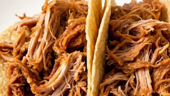 A close-up of finished Mexican shredded turkey tacos on a white plate with a blurry kitchen background.