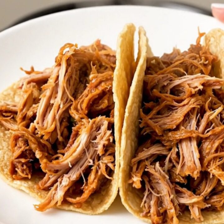 A close-up of finished Mexican shredded turkey tacos on a white plate with a blurry kitchen background.