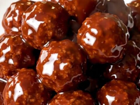 Glossy, glazed meatballs in a slow cooker on a white speckled quartz countertop.