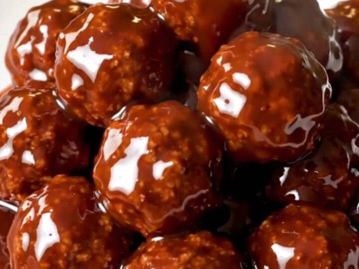 Glossy, glazed meatballs in a slow cooker on a white speckled quartz countertop.