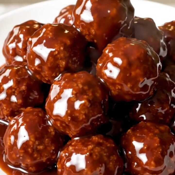 Glossy, glazed meatballs in a slow cooker on a white speckled quartz countertop.