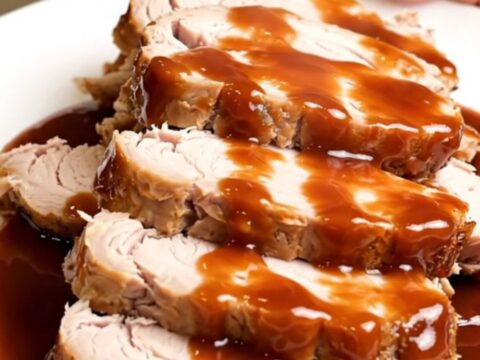 A plate of sliced, glossy barbecue-glazed turkey tenderloin with bacon bits, steaming slightly.