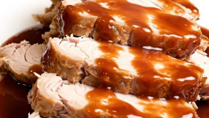 A plate of sliced, glossy barbecue-glazed turkey tenderloin with bacon bits, steaming slightly.