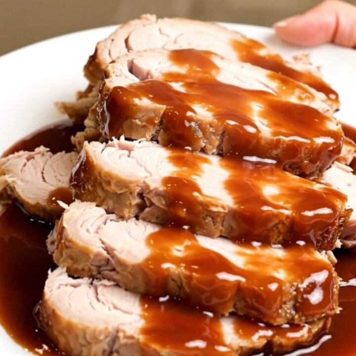 A plate of sliced, glossy barbecue-glazed turkey tenderloin with bacon bits, steaming slightly.