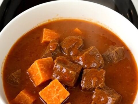 A rustic bowl of slow-cooked beef and sweet potato stew with a rich, glossy broth.