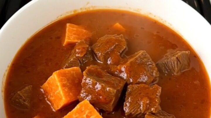 A rustic bowl of slow-cooked beef and sweet potato stew with a rich, glossy broth.