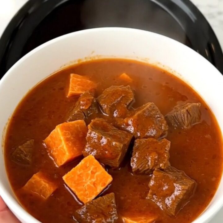 A rustic bowl of slow-cooked beef and sweet potato stew with a rich, glossy broth.