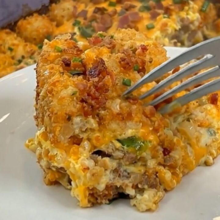 A slice of loaded tater tot breakfast casserole on a white plate with melted cheese and crispy edges.