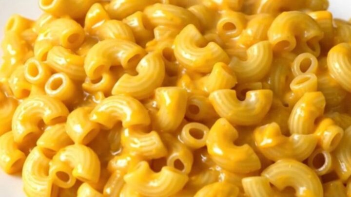 A top-down view of a slow cooker filled with creamy cheddar macaroni, diced apples, and a touch of apple cider.