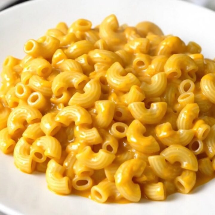A top-down view of a slow cooker filled with creamy cheddar macaroni, diced apples, and a touch of apple cider.