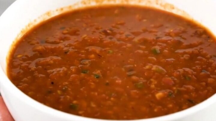 A white ceramic bowl filled with rich, steaming chorizo and bean chili on a wooden table.