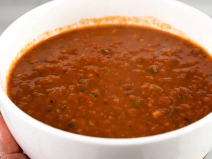 A white ceramic bowl filled with rich, steaming chorizo and bean chili on a wooden table.