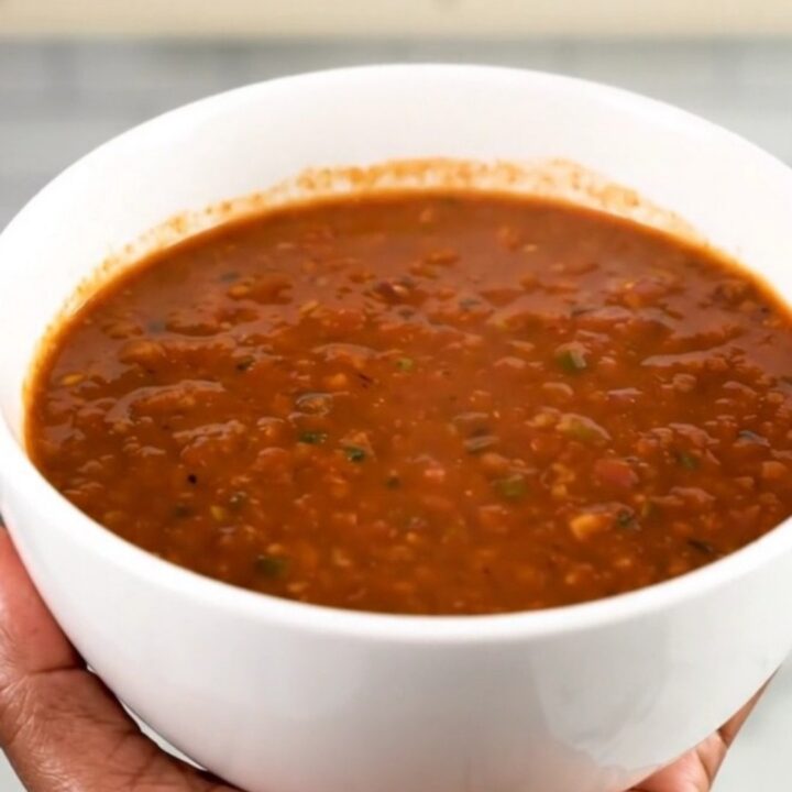 A white ceramic bowl filled with rich, steaming chorizo and bean chili on a wooden table.