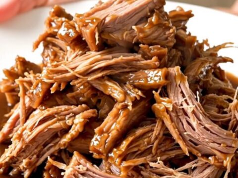 A slow cooker filled with a large, tender pork shoulder roast seasoned with onions and five-spice sauce.
