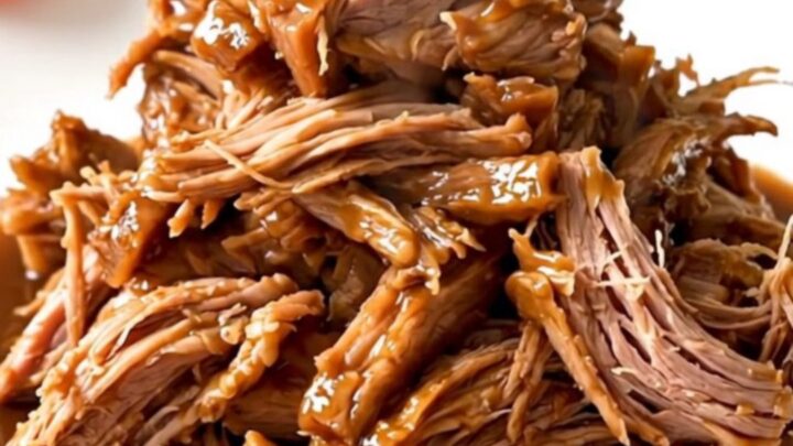 A slow cooker filled with a large, tender pork shoulder roast seasoned with onions and five-spice sauce.