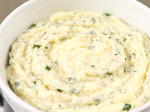 A glossy, creamy white cheddar dip in a white bowl with fresh herbs.